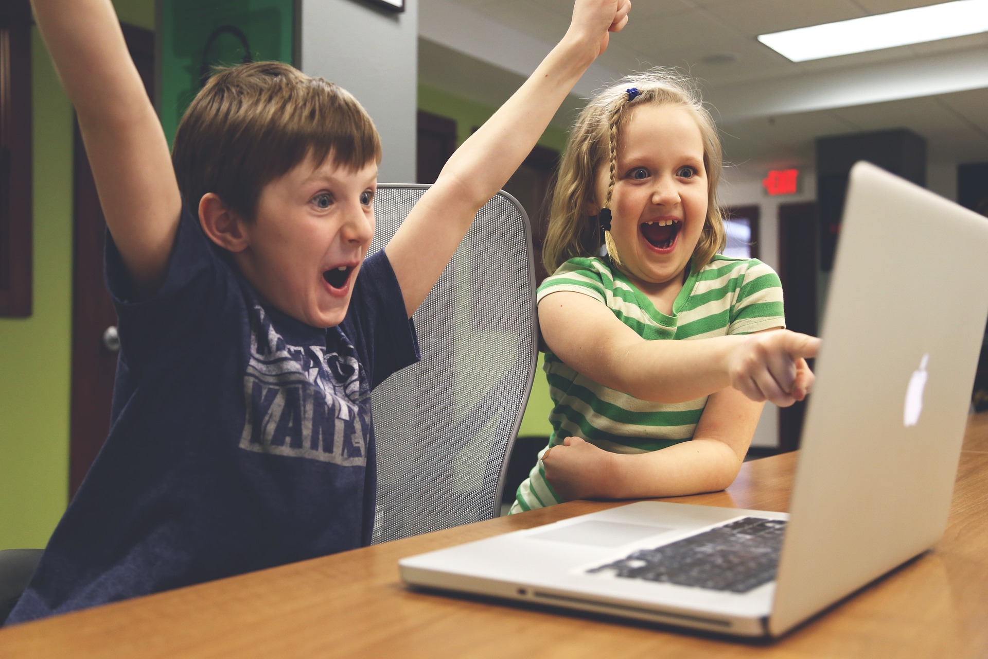 zwei Kinder sitzen jubelnd vor einem Laptop