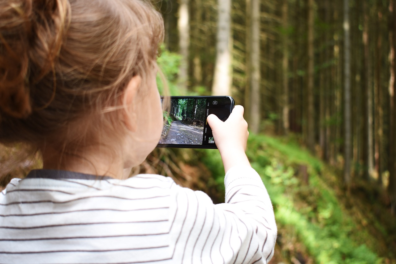 Kind mir Handy in der Hand fotografiert im Wald.